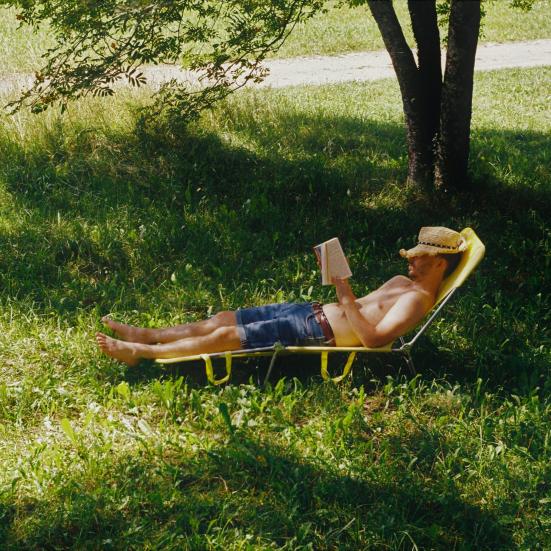 Mand der ligger i skyggen af et træ og læser en bog