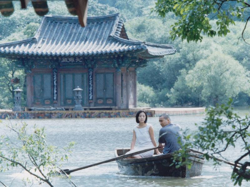 Mand og kvinde i en båd på en sø, foran et koreansk hus.