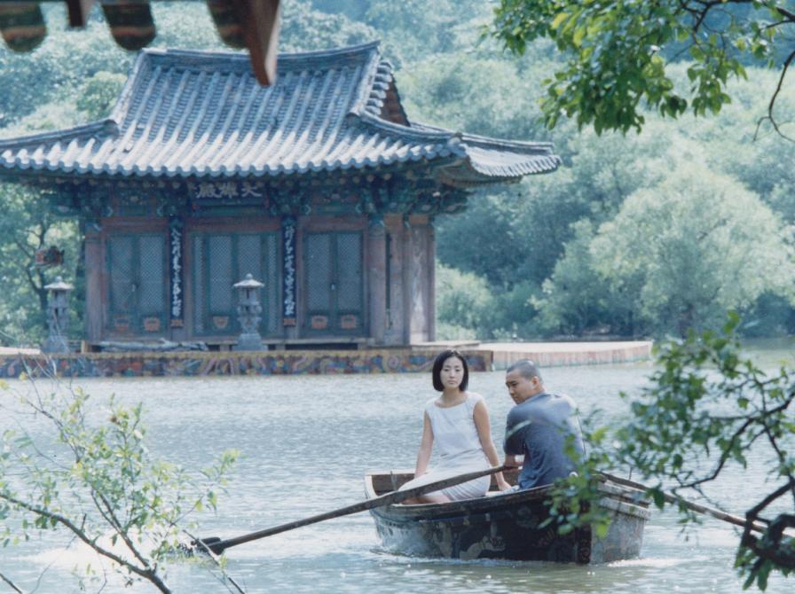 Mand og kvinde i en båd på en sø, foran et koreansk hus.